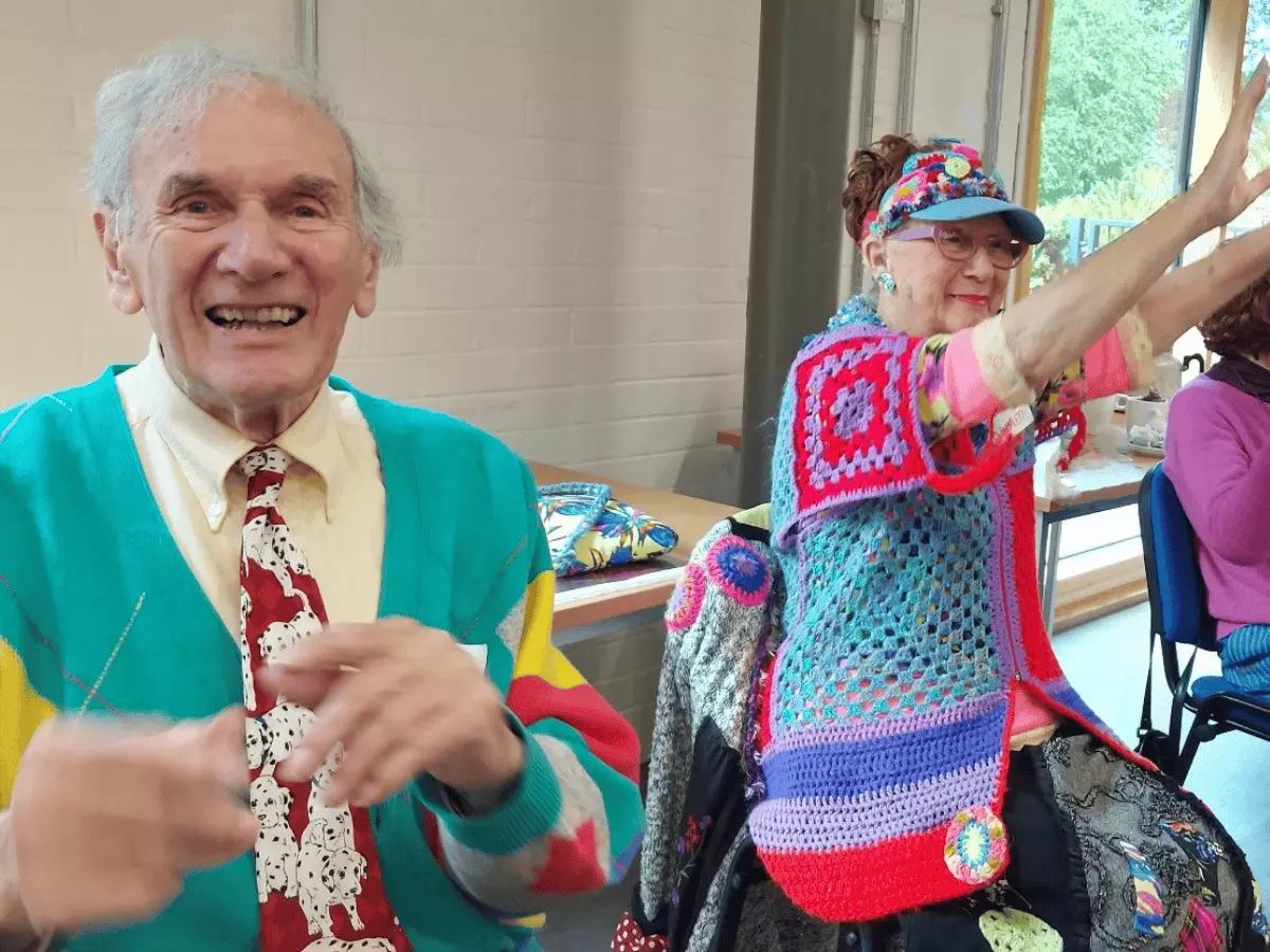 Man and woman in bright clothing dancing and smiling at the camera