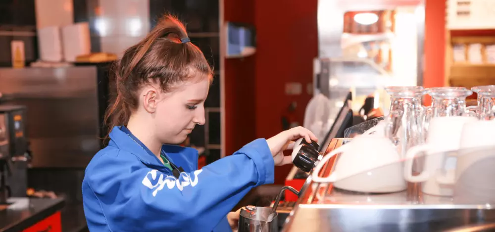 A woman operating a coffee machine in bright blue overalls.