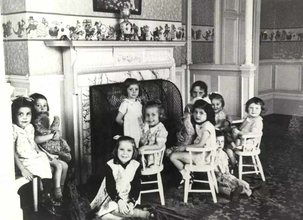 An old black and white photo of a group of little girls sitting around a fireplace at Strawberry Field.