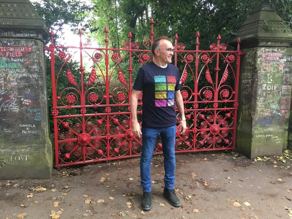 Danny Boyle standing outside the red Strawberry Field gates.