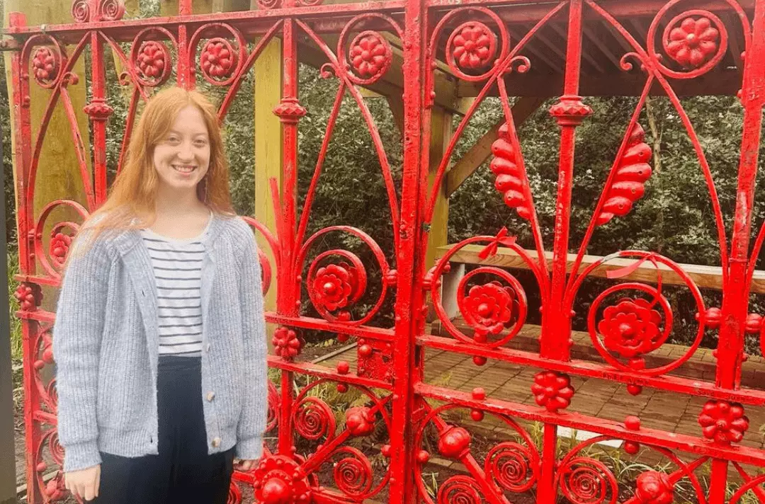 LJMU student intern standing smiling outside the red gates of Strawberry Fields