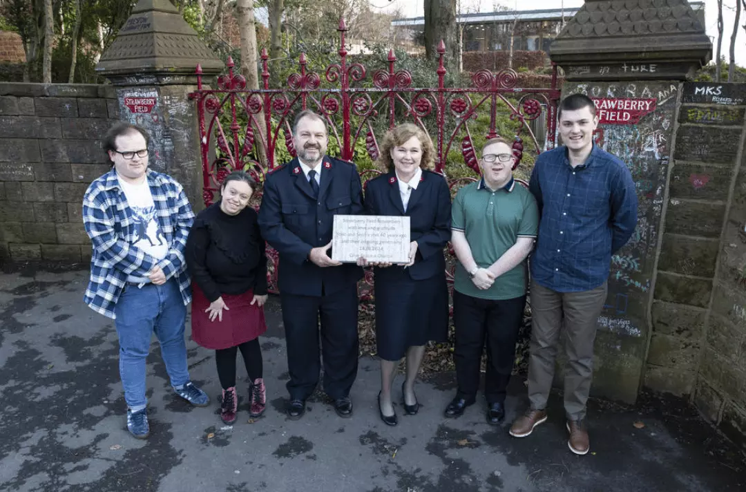 Majors Allister & Kathy Versfeld stand with Steps to Work trainees holding a stone commemorating Yoko & Sean Ono Lennon's visit in 1984 in front of the Strawberry Field