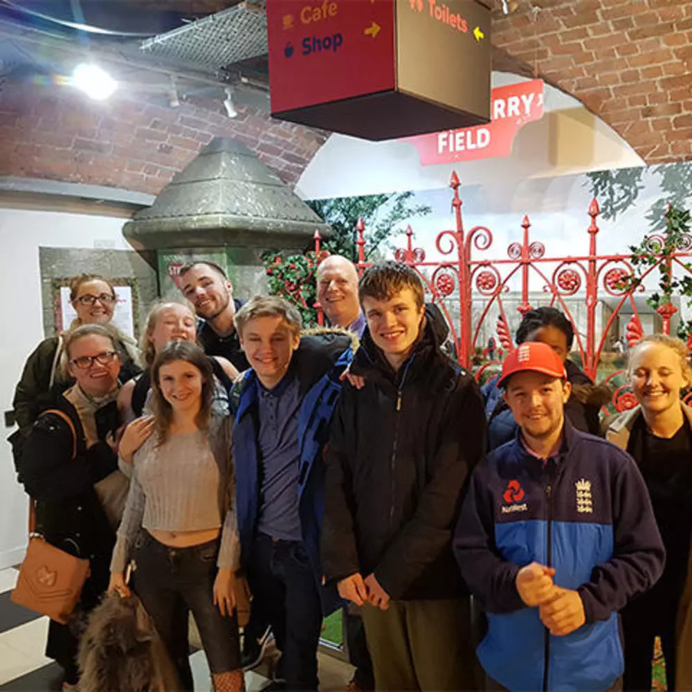 8 young adults standing in front of the red Strawberry Field gates.