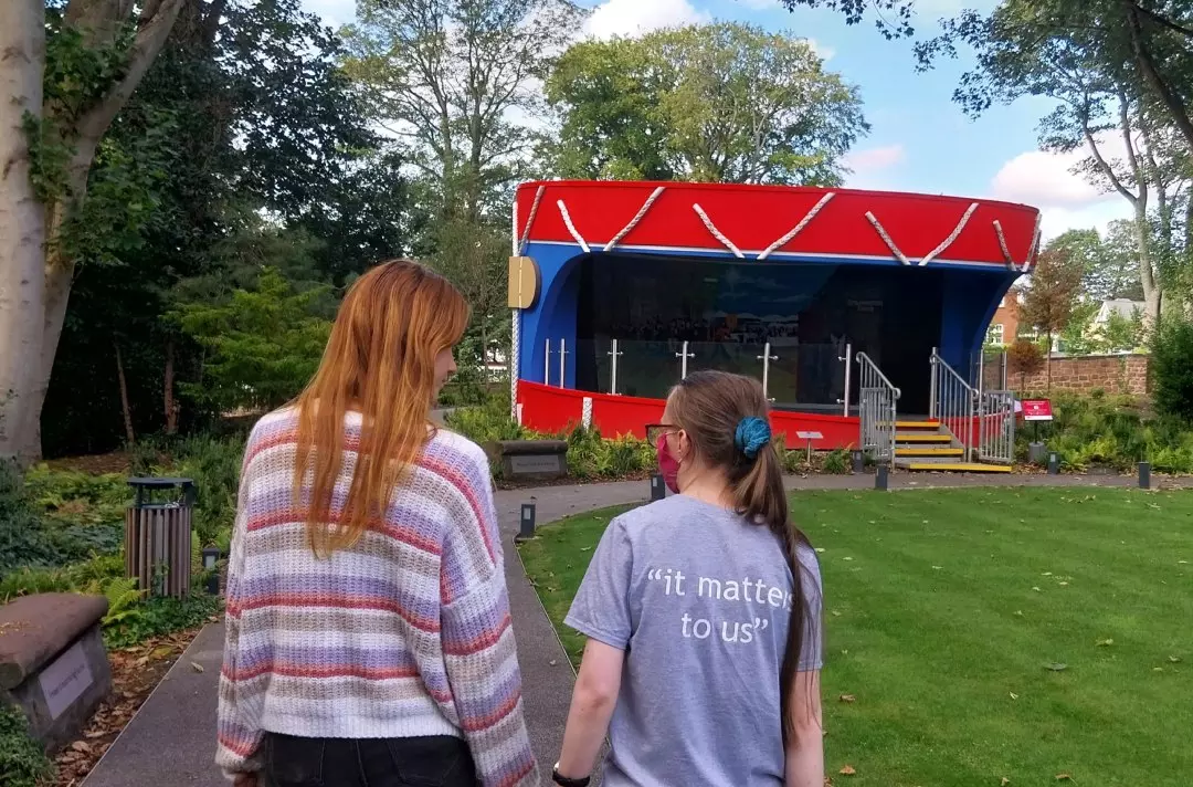 Two people stand facing a red and blue bandstand in gardens at Strawberry Field