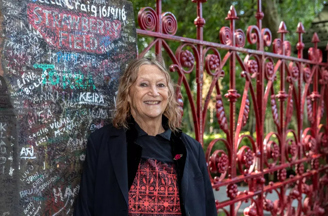 Julia Baird, standing in front of the iconic red gates at Strawberry Field