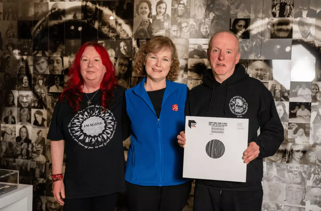 Major Kathy Versfeld stands between Paula and Tony Quinn of the Musical Box record shop. Tony holds a vinyl acetate of Happy Xmas (War is Over)
