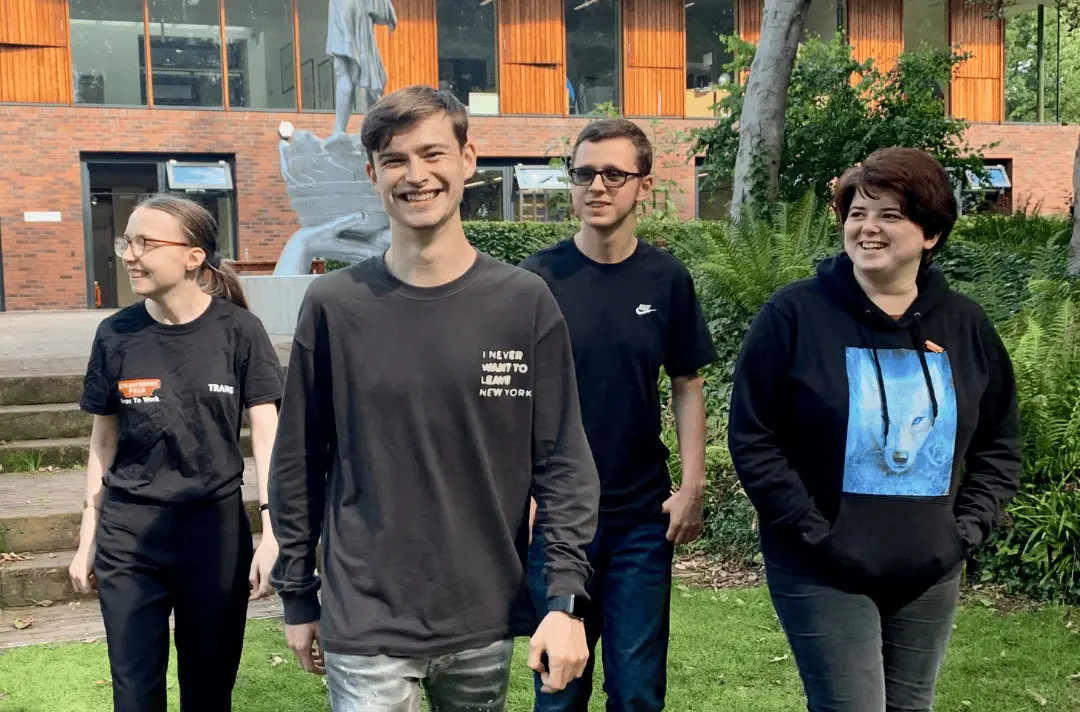 Four young people walk in the Strawberry Field garden, smiling.