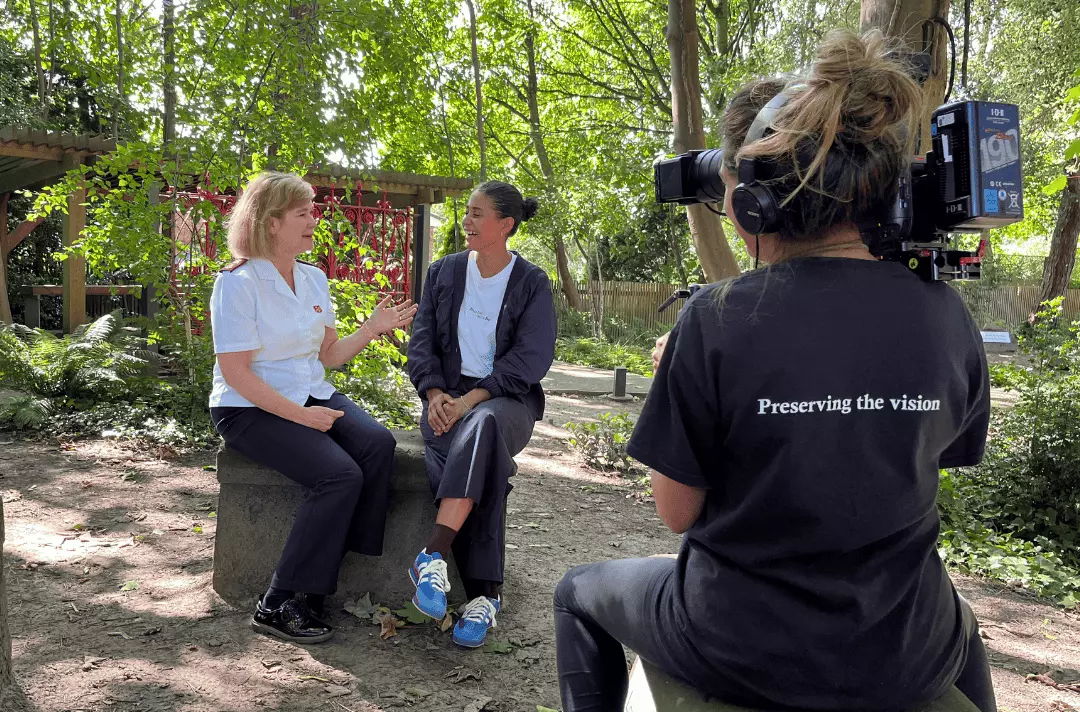Major Kathy Versfeld sits with chef Liv Alarcon in front of the original Strawberry Field gates, being filmed by a camerawoman