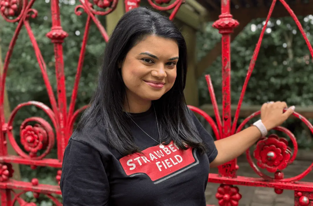 Hema, a woman with black hair and brown skin, stands by the Strawberry Field gates.