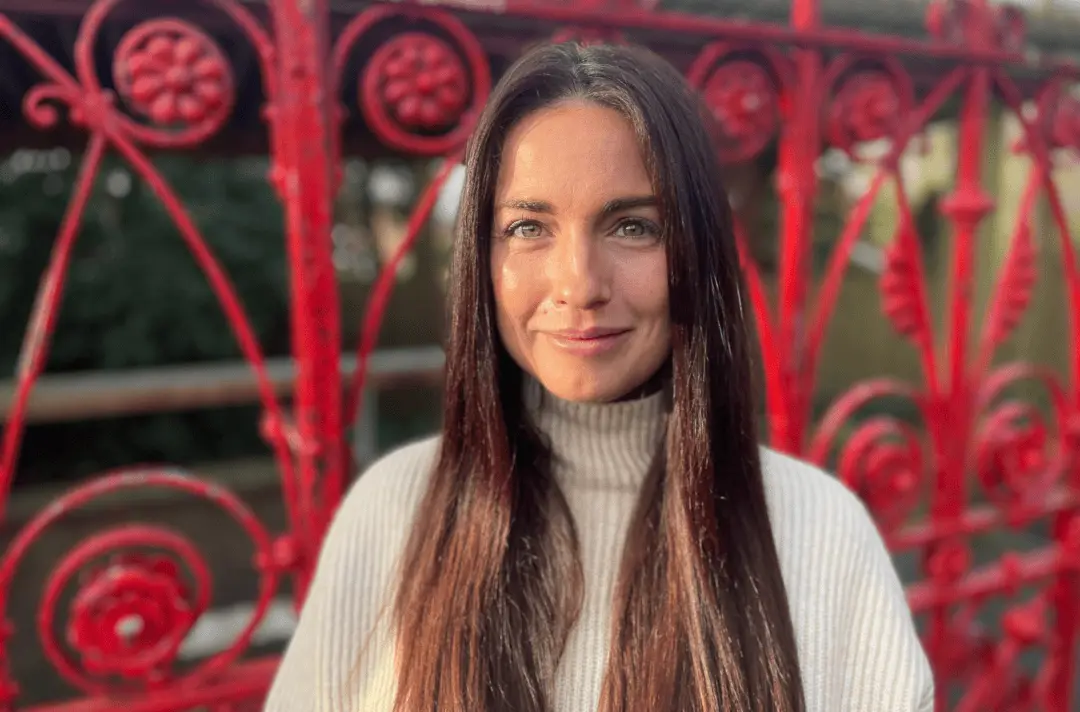 A woman with long brunette hair wearing a cream polo neck jumper.