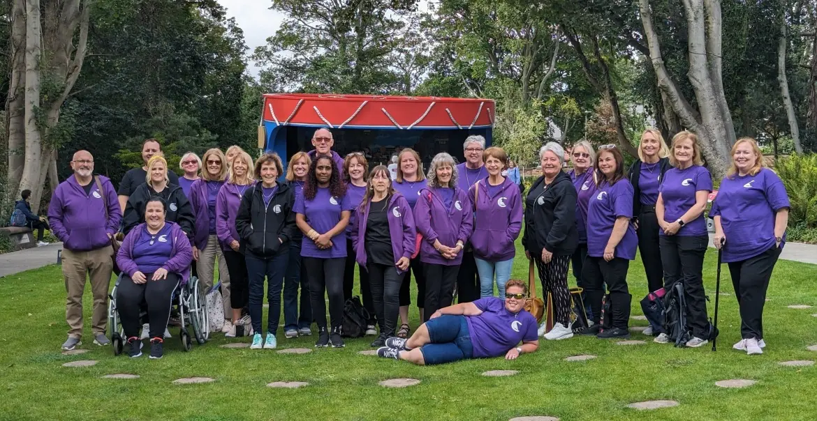 Wall of Sound choir stand in front of the Strawberry Field bandstand wearing matching purple tops and fleeces.