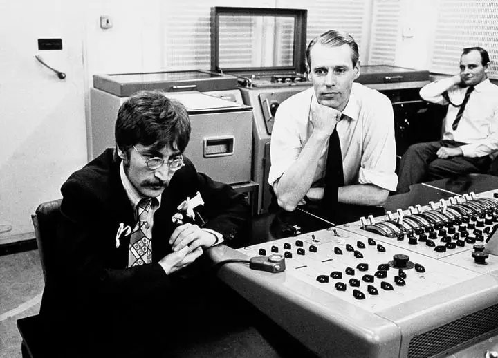 Black and white photograph and John Lennon and George Martin leant over a mixing desk