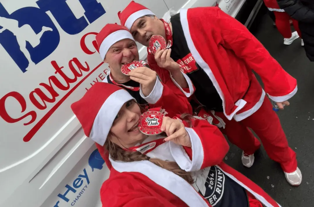 Three people dressed as Father Christmas bite red 'Santa Dash 5k' medals