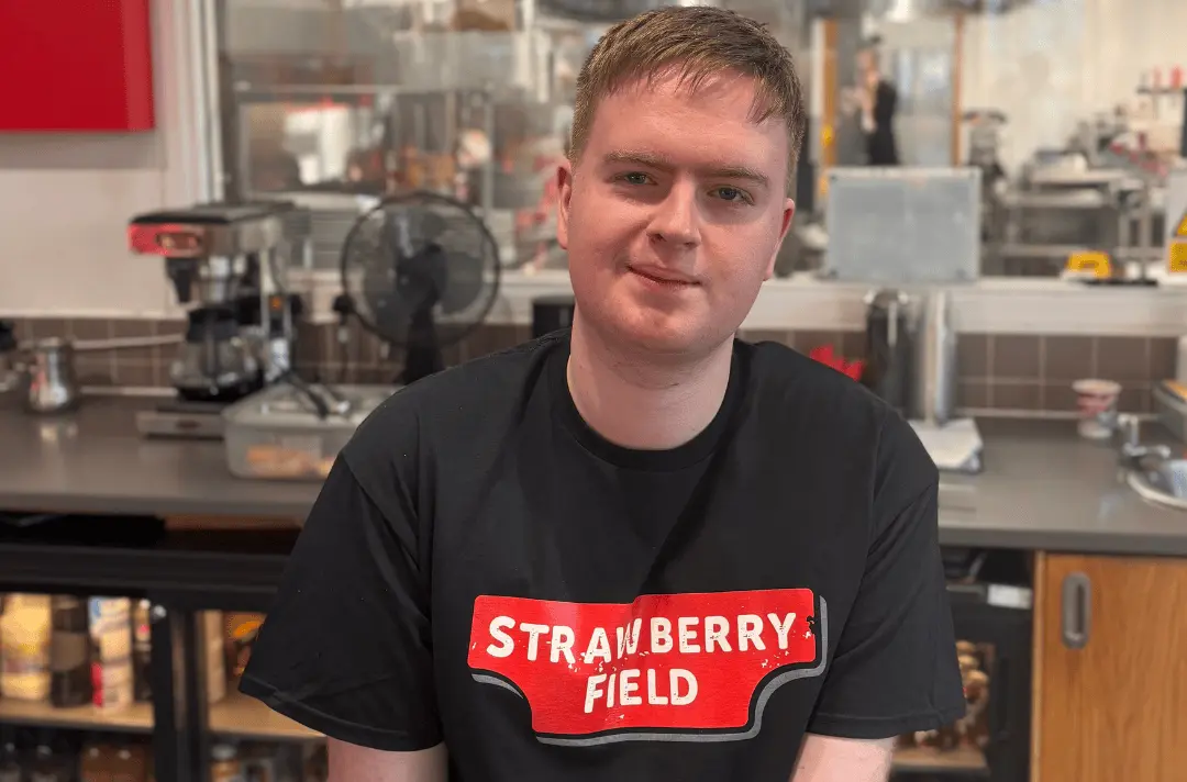 Jonathan, a trainee on the Steps to Work programme, stands behind the counter in the Imagine More cafe wearing a Strawberry Field tshirt